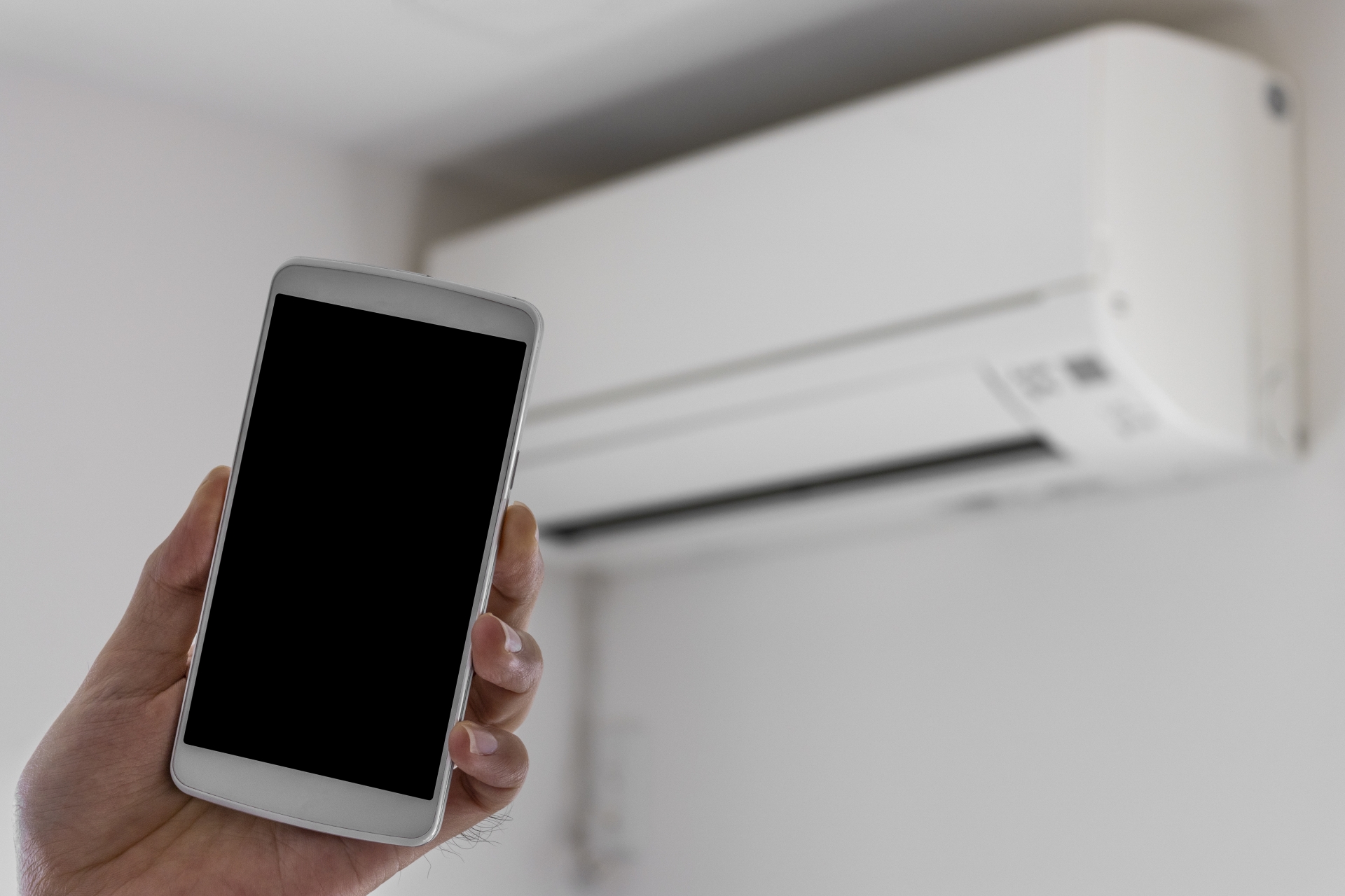 スマートフォンでエアコンを遠隔操作している様子。スマート家電による快適なひとり暮らしをイメージ